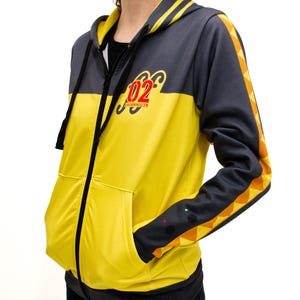 May include: A yellow and black zip-up hoodie with a black and orange stripe down the sleeve. The hoodie has a large number "02" with the text "Karaminilen" printed on the front.