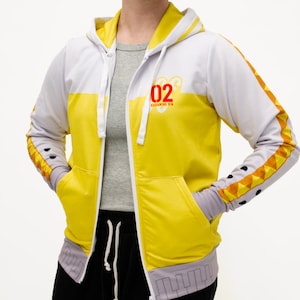 May include: A white and yellow zip-up hoodie with a red and black "02" logo on the front. The hoodie has a grey hood and a grey drawstring. The sleeves have a black and yellow geometric pattern.