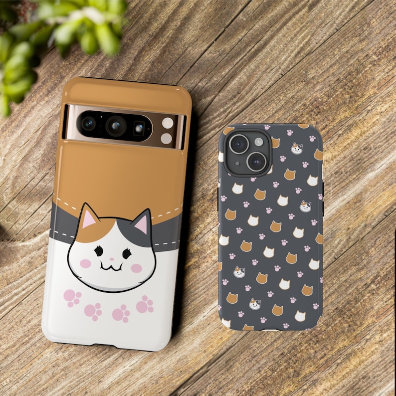 May include: Two phone cases with a cat design. The first case is brown with a white cat face and pink paw prints. The second case is black with a repeating pattern of white cat faces and pink paw prints.