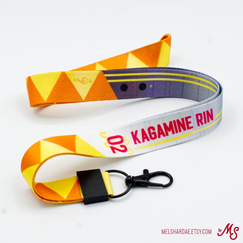 May include: A white, yellow, and orange lanyard with a black and gray pattern and the text "202 Kagamine Rin" printed on it. The lanyard has a black breakaway clasp and a silver metal hook.
