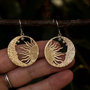 May include: A pair of gold-toned earrings featuring a hammered crescent moon design with a sun cutout and three small stars.