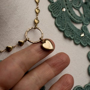 May include: A gold necklace with a heart charm and a circle pendant. The necklace is made of small heart-shaped links.