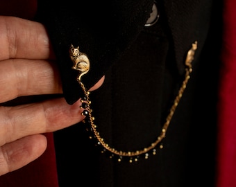 May include: A gold chain with black beads and a small gold cat charm attached to a black shirt collar.