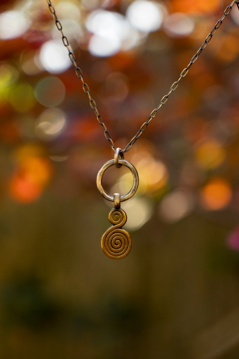 Puede incluir: Un collar de cadena dorada con un colgante que presenta un c&iacute;rculo y un dise&ntilde;o de doble espiral.