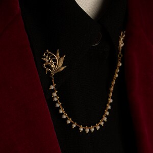 May include: A gold chain with lily flower charms and white beads, worn as a collar accessory.