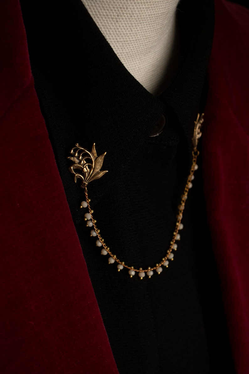 May include: A gold chain with lily flower charms and white beads, worn as a collar accessory.