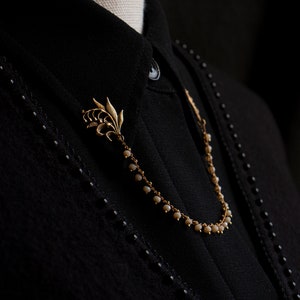 May include: A gold chain necklace with a lily flower charm and small white beads. The necklace is on a black shirt.