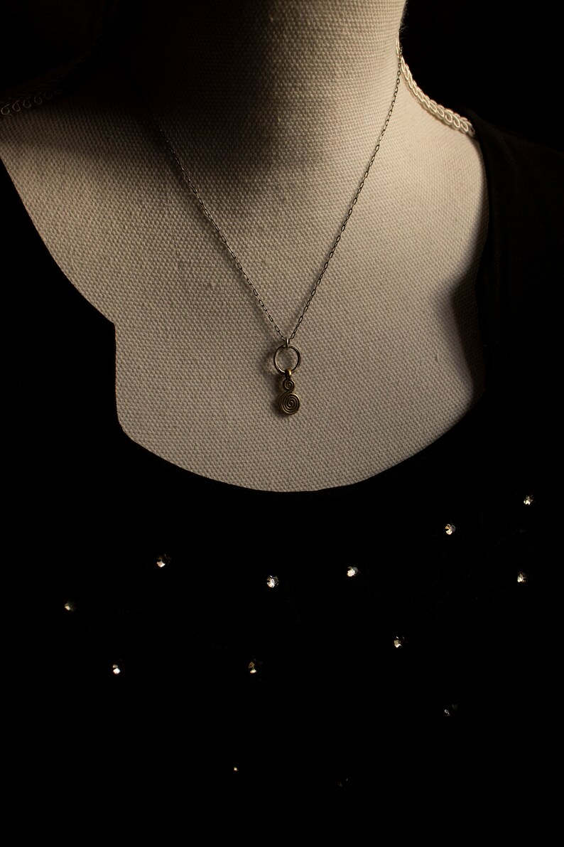 Puede incluir: Un collar de cadena de plata con un peque&ntilde;o colgante de c&iacute;rculo dorado y un dise&ntilde;o en espiral.