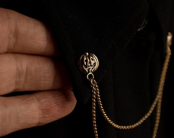 May include: A gold chain with a pumpkin-shaped charm attached to a black shirt collar.