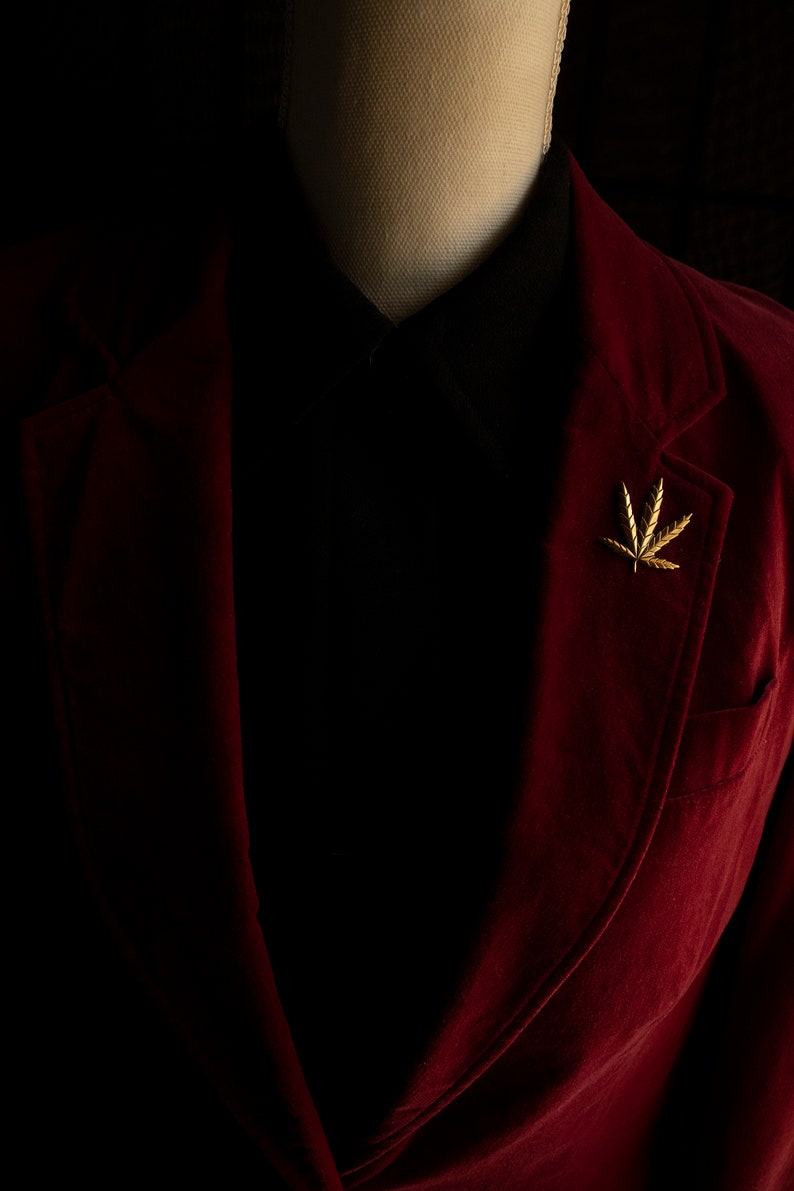 Pode incluir: Um blazer de veludo vermelho com um broche de folha de ouro na lapela.
