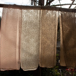 Op de afbeelding: Vier doorschijnende sjaals met een bruin en wit stippenpatroon hangen aan een houten stok.