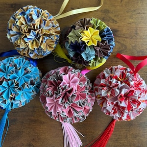 Puede incluir: Cinco adornos esféricos hechos de papel plegado, cada uno con intrincados patrones geométricos y colores vibrantes que incluyen azul, dorado, amarillo, rosa y rojo. Cada adorno tiene una cinta para colgar y una borla colgante a juego.