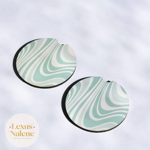 May include: Two round green and white swirl patterned coasters with a cut-out for a cup.