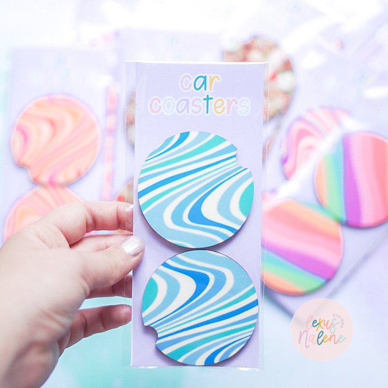 Pode incluir: Dois porta-copos para carro com um padr&atilde;o de redemoinho azul e branco. Os porta-copos est&atilde;o em uma manga de pl&aacute;stico transparente com o texto "car coasters" na embalagem.