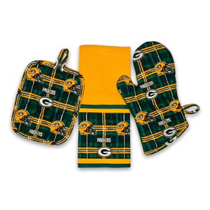 May include: Green Bay Packers kitchen towel set with a green and yellow plaid pattern featuring the team logo and the words "Packers". The set includes a potholder, oven mitt, and a kitchen towel.