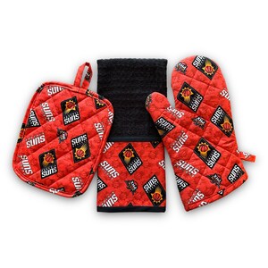 May include: A red and black kitchen towel set with a Phoenix Suns logo pattern. The set includes a potholder, oven mitt, and a dish towel.