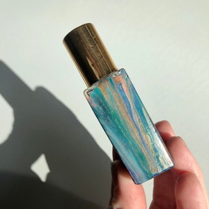 May include: A small glass bottle with a gold cap and a blue, green, and gold marbled design.