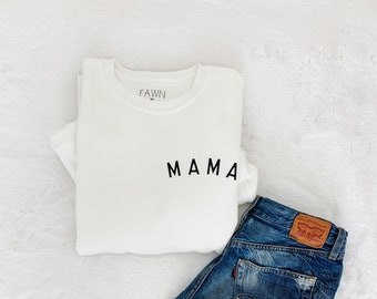 May include: White sweatshirt with the word "MAMA" printed on the front, paired with blue denim shorts.