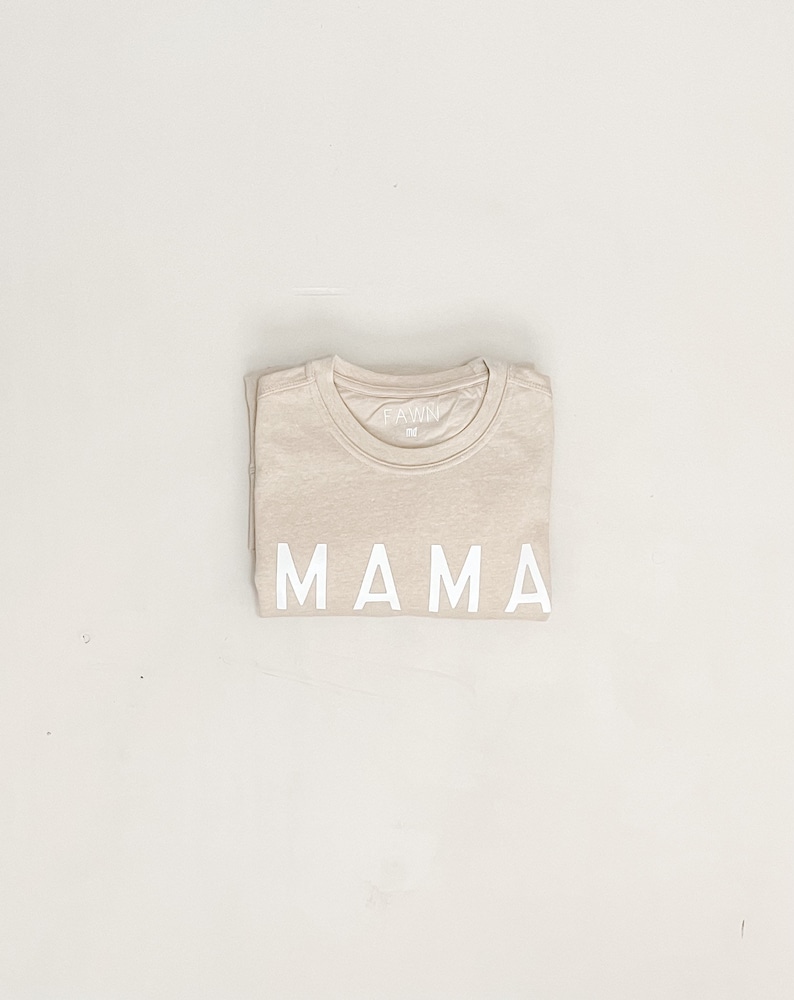 K&ouml;nnte beinhalten: Ein beiges T-Shirt mit dem Wort "MAMA" in wei&szlig; auf der Vorderseite.