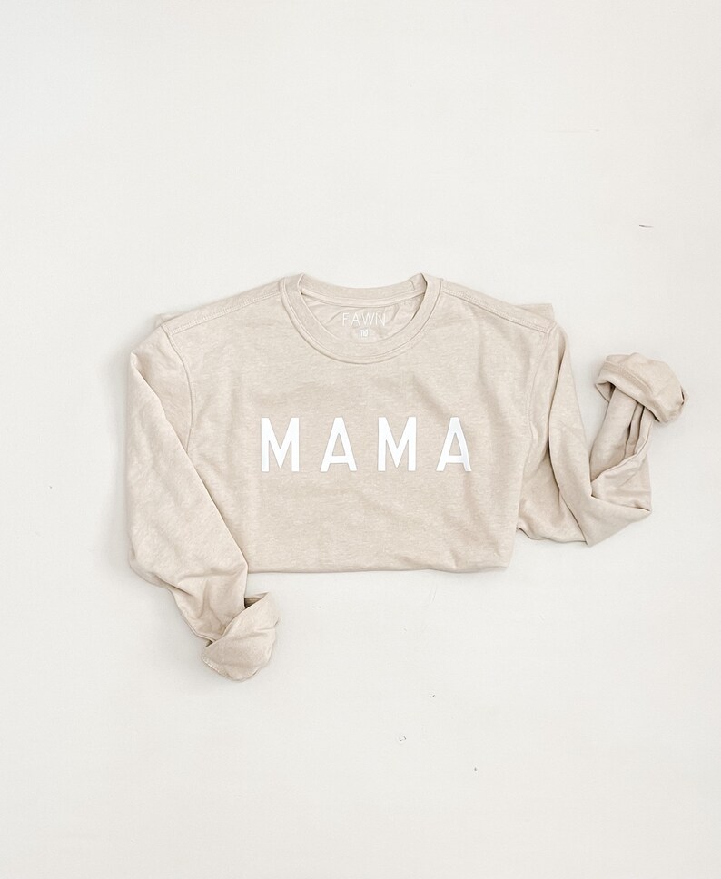 K&ouml;nnte beinhalten: Ein beiger Langarmsweater mit dem Wort "MAMA" in wei&szlig; auf der Vorderseite.