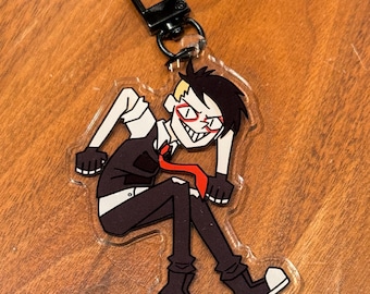 May include: A clear acrylic keyring featuring a cartoon character in a black suit, red tie, and black boots. The character has spiky black hair, red-rimmed glasses, and a mischievous expression. The keyring has a black metal clasp.