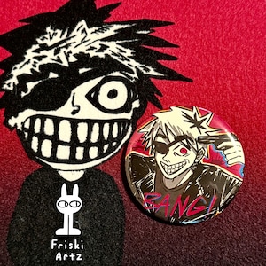May include: A round button with a cartoon illustration of a character with a black eye patch, spiky hair, and the word "BANG!" in red. The button is on a red background with a black and white cartoon character.