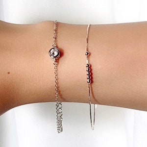 May include: A silver bracelet with a single clear crystal charm and a silver chain bracelet with small beads.