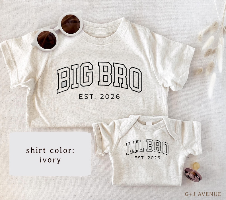Puede incluir: Camisetas color marfil, una para adulto y otra para beb&eacute;, con texto negro. La camiseta de adulto dice "BIG BRO EST. 2026", mientras que la camiseta de beb&eacute; dice "LIL BRO EST. 2026". Gafas de sol blancas sobre la camiseta de adulto.