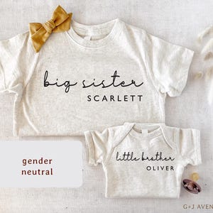 May include: Two light gray baby shirts, one with "big sister SCARLETT" and a mustard bow, the other with "little brother OLIVER". A pacifier is next to the smaller shirt. The words "gender neutral" are in a white box.
