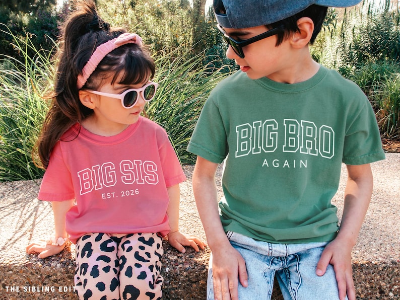 Puede incluir: Dos ni&ntilde;os con gafas de sol y camisetas a juego. La camiseta de la ni&ntilde;a es rosa y dice "BIG SIS EST. 2026". La camiseta del ni&ntilde;o es verde y dice "BIG BRO AGAIN". Est&aacute;n al aire libre.