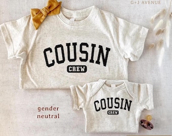 May include: Ivory-colored t-shirts and a onesie with the words "COUSIN CREW" in black block letters. A mustard-colored bow is pinned to the top shirt. The text "gender neutral" is printed on the bottom left.