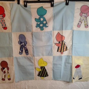 May include: A patchwork quilt featuring nine squares with appliqued figures. The figures are in various colors and patterns, including red, blue, pink, and yellow. The background is a mix of white and light blue squares, creating a vintage aesthetic.