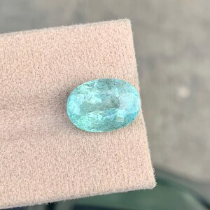 Peut inclure: Une pierre pr&eacute;cieuse &agrave; facettes de forme ovale, d'une couleur bleu-vert translucide. La pierre pr&eacute;sente des inclusions internes et une surface r&eacute;fl&eacute;chissante, mettant en valeur une taille brillant avec de multiples facettes lumineuses.