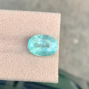 Peut inclure: Une pierre pr&eacute;cieuse &agrave; facettes de forme ovale, d'une couleur bleu turquoise clair translucide. La pierre pr&eacute;sente des inclusions internes et une surface r&eacute;fl&eacute;chissante, r&eacute;v&eacute;lant un m&eacute;lange de teintes vert p&acirc;le et bleu sur toute sa structure polie.