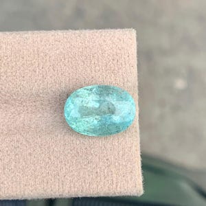 Peut inclure: Une pierre pr&eacute;cieuse &agrave; facettes de forme ovale, d'une couleur bleu-vert translucide. La pierre pr&eacute;sente une surface polie avec des inclusions internes visibles et une taille brillant qui refl&egrave;te la lumi&egrave;re sur ses bords arrondis.