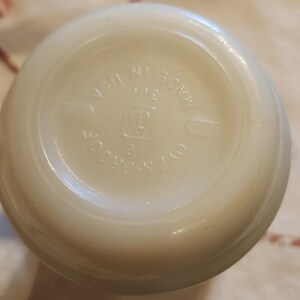 Puede incluir: Primer plano de la parte inferior de un tarro de vidrio blanco con el texto "MADE IN USA" y un logotipo que parece una "G" estilizada dentro de un cuadrado.