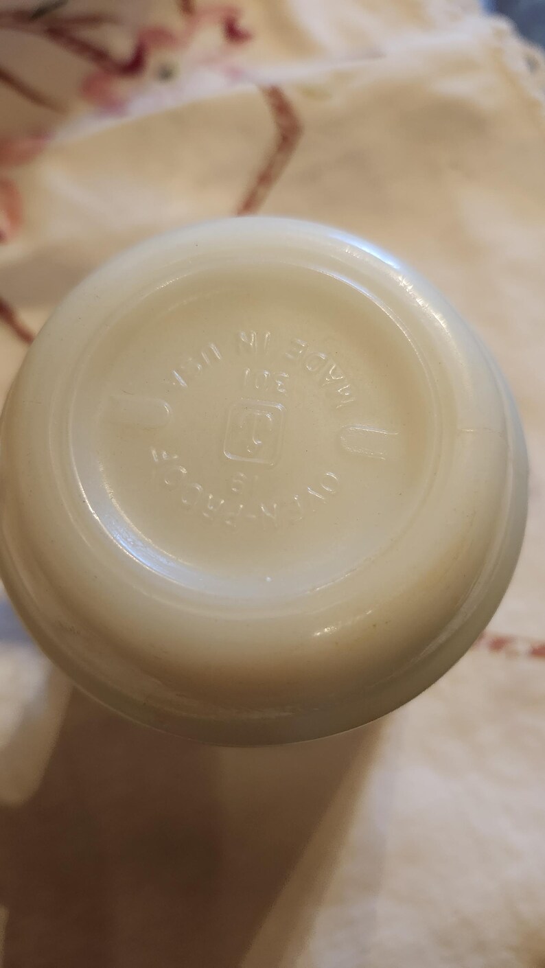 Puede incluir: Primer plano de la parte inferior de un tarro de vidrio blanco con el texto "MADE IN USA" y un logotipo que parece una "G" estilizada dentro de un cuadrado.