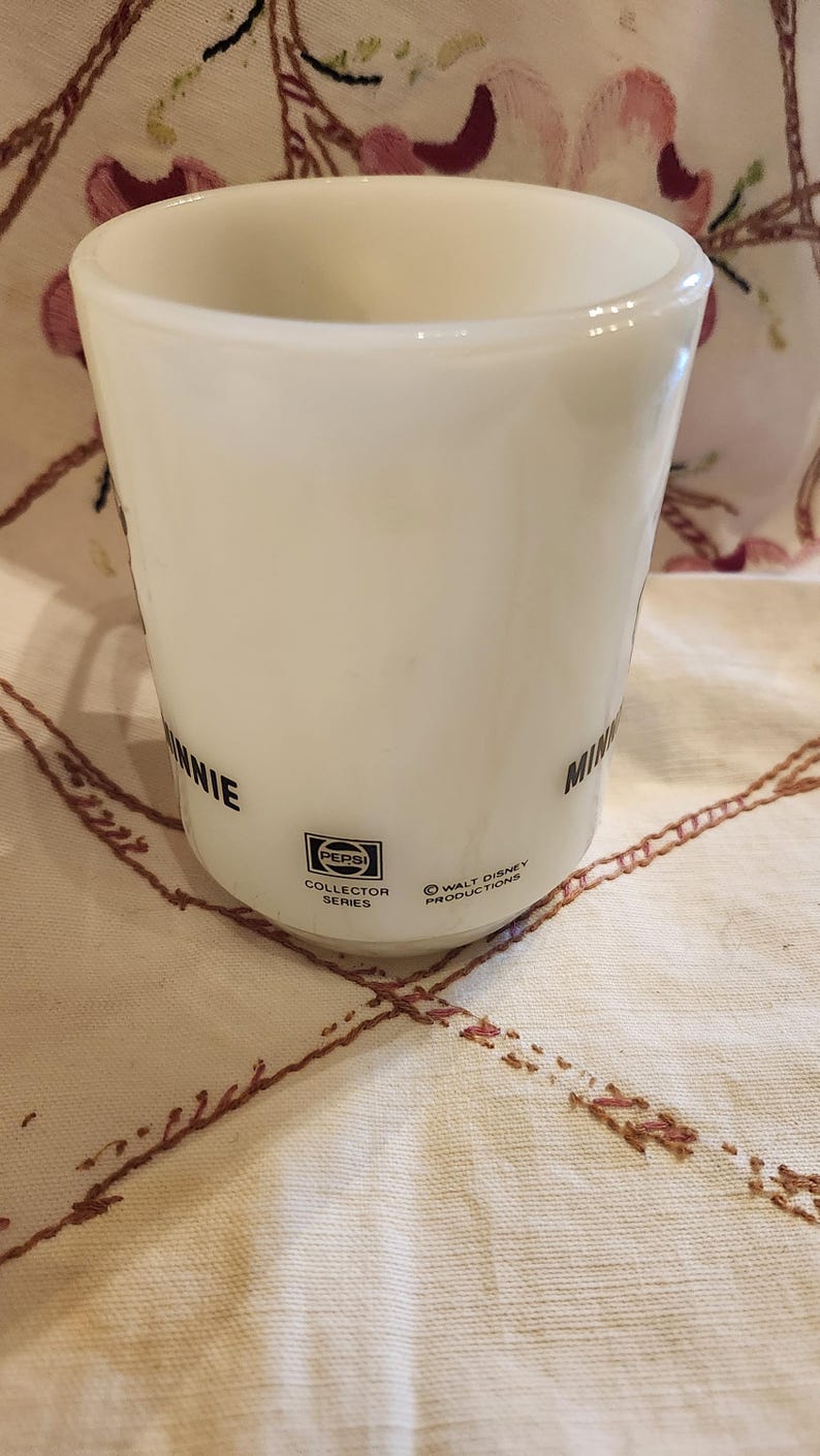 Puede incluir: Taza de cer&aacute;mica blanca con texto negro que dice "Minnie Mouse" y "Pepsi Collector Series" con un logotipo de Pepsi. La taza tambi&eacute;n tiene el texto "Walt Disney Productions" en la parte inferior.