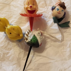 May include: Four vintage cake toppers, including a clown with a red nose and a blue hat, a turkey with green and white feathers, a yellow chick, and a doll with a red and white striped hat and blue eyes.