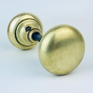 Puede incluir: Un par de pomos de puerta antiguos de latón. Los pomos son redondos con una superficie lisa y pulida y un tono dorado cálido. La ferretería está montada sobre una varilla de metal oscuro, y el diseño es clásico y atemporal.