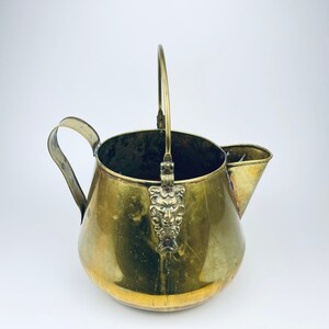 May include: A brass pitcher with a handle and a spout. The pitcher has a decorative design on the handle.