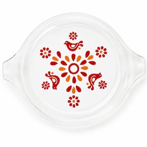 May include: A clear glass lid with two side handles, featuring a central graphic pattern of red and orange stylized birds and flowers arranged in a circular motif. The design is printed on the surface of the transparent glass cookware cover.