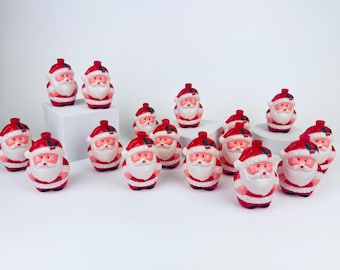 May include: A collection of small, red and white Santa Claus figurines. Each figurine has a red hat, a white beard, and a red and white striped suit. The figurines are arranged on a white surface.