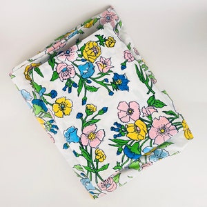 Pode incluir: Lençóis brancos dobrados com um padrão floral em rosa, amarelo e azul. O desenho inclui caules e folhas verdes. Os lençóis são feitos de tecido macio. O padrão floral adiciona um toque de cor a um quarto.