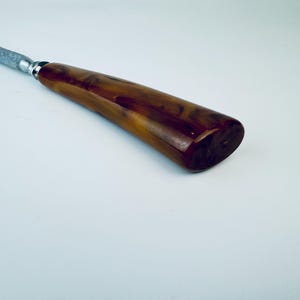 May include: A close-up of a brown and black handled knife sharpener. The handle is made of a marbled plastic material.