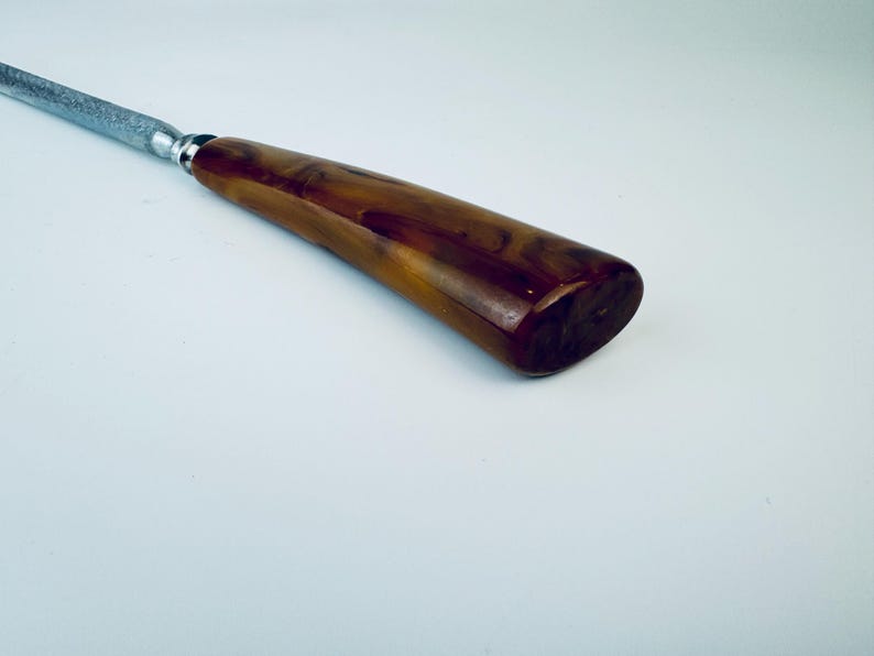 May include: A close-up of a brown and black handled knife sharpener. The handle is made of a marbled plastic material.