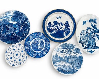 Puede incluir: Una colección de cinco platos de cerámica con patrones de transferencia en azul y blanco. Los diseños incluyen paisajes pastorales, escenas arquitectónicas, motivos florales y una fuente ovalada con una ilustración de árbol y ave sobre fondo blanco.