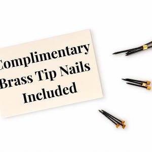 May include: A cream-colored card with the text "Complimentary Brass Tip Nails Included" next to three black nails with gold-colored tips. The nails are arranged on a white background.
