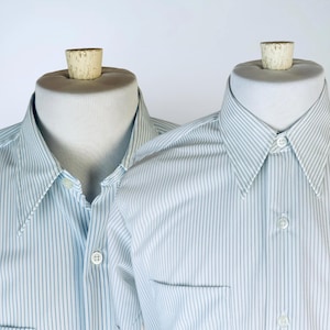 May include: Two white dress shirts with thin blue stripes. The shirts have a button-down collar and a single button cuff.