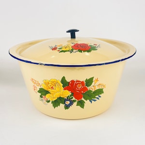 May include: Cream-colored enamelware bowl with a matching lid. The bowl is decorated with floral designs in yellow, red, and green. The rim is trimmed with a blue border. A black knob is on top of the lid.